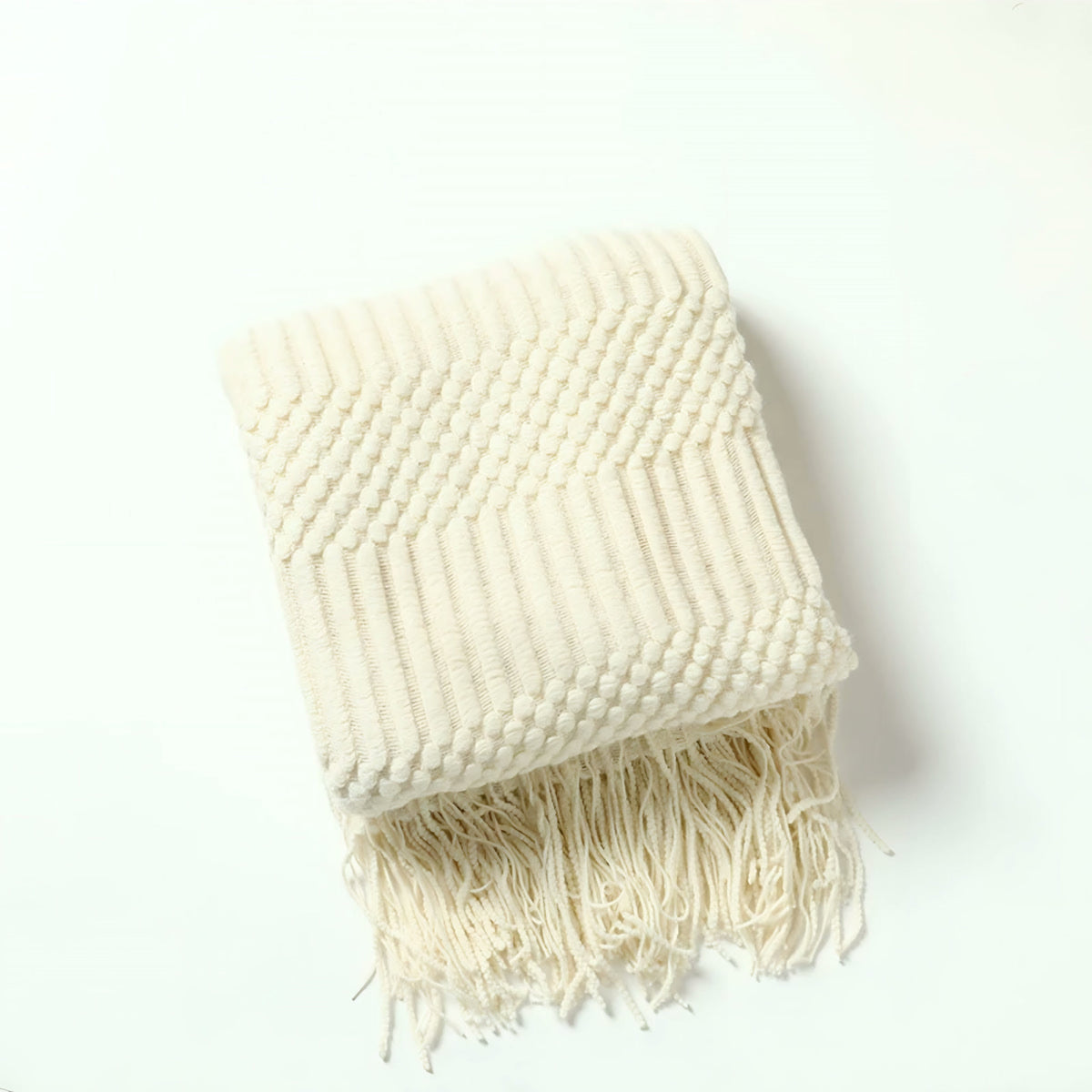 Plaid tricoté écru plié sur fond clair, maille gaufrée en relief et franges nouées