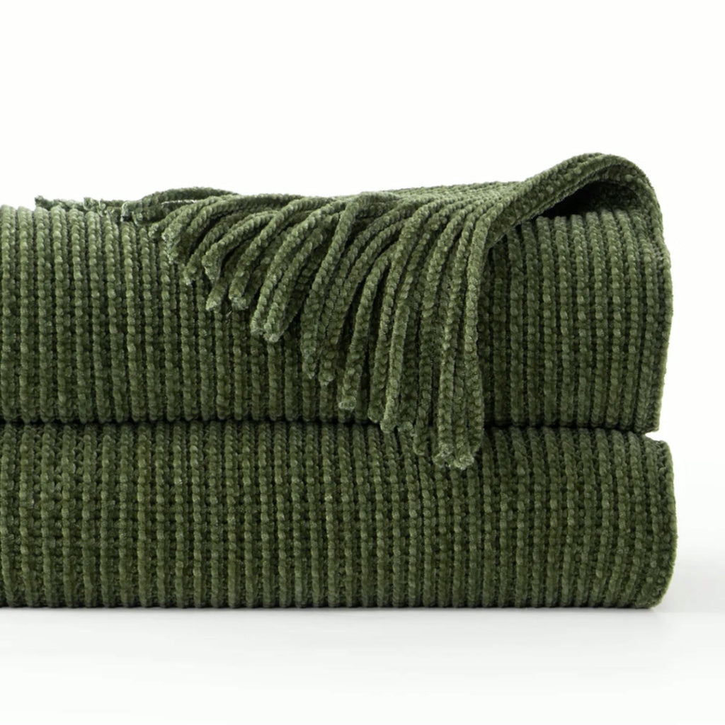 Plaid tricoté vert sapin plié sur fond blanc, maille côtelée et franges en chenille