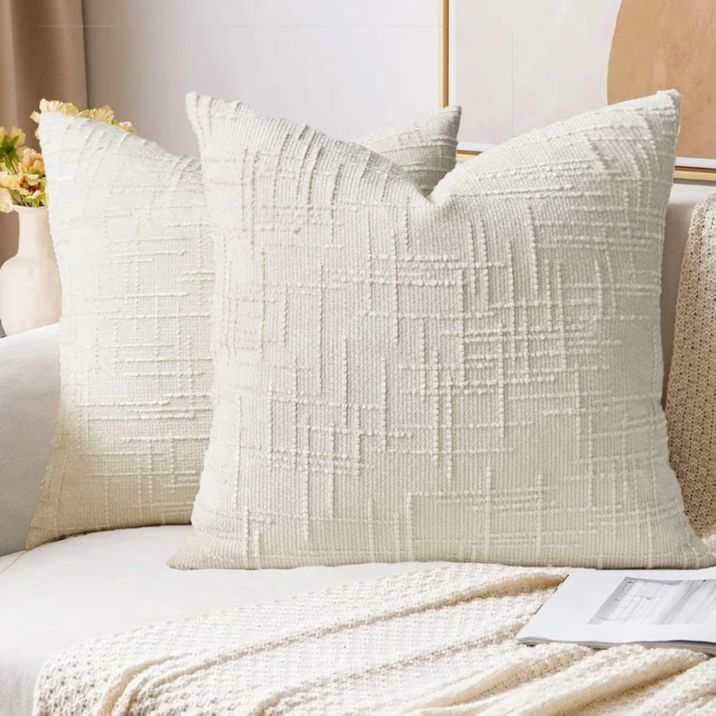 Deux housses de coussin en chenille écru sur un canapé clair, motif en relief