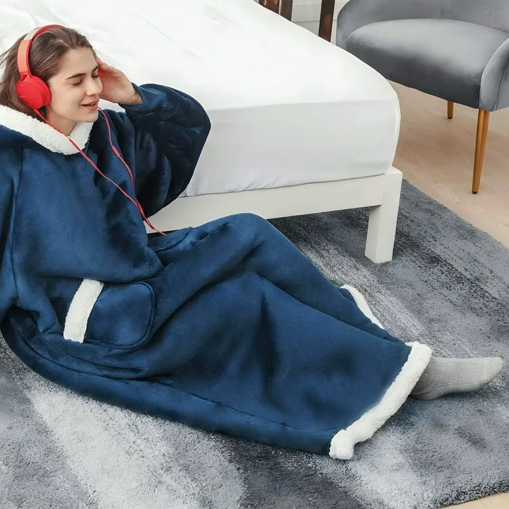 Femme assise sur un tapis, enveloppée dans le plaid à manches bleu nuit, capuche bordée sherpa