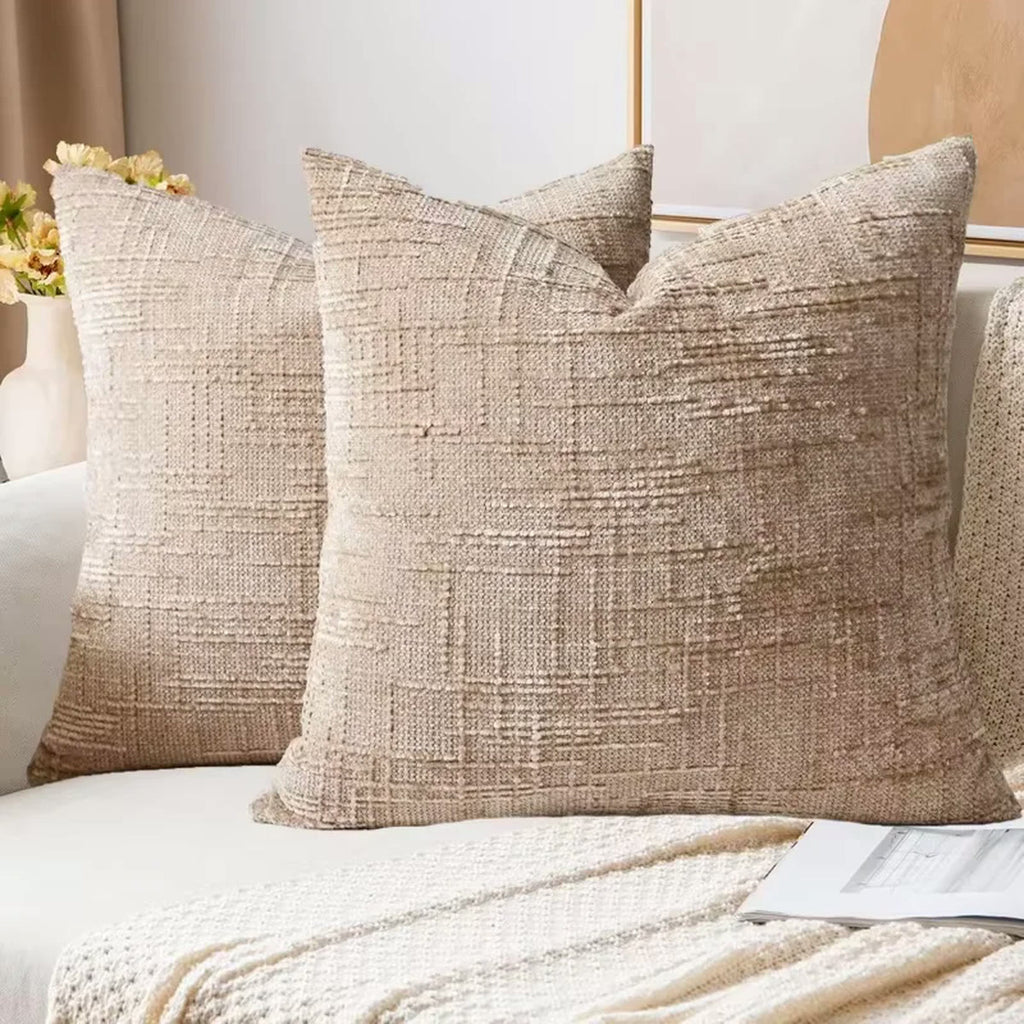 Deux housses de coussin en chenille camel clair sur un canapé, plaid tricoté au premier plan