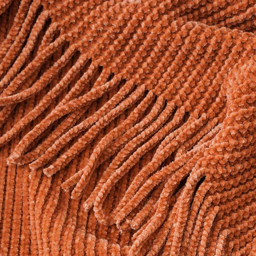 Gros plan de la maille chenille terracotta et des franges du plaid tricoté