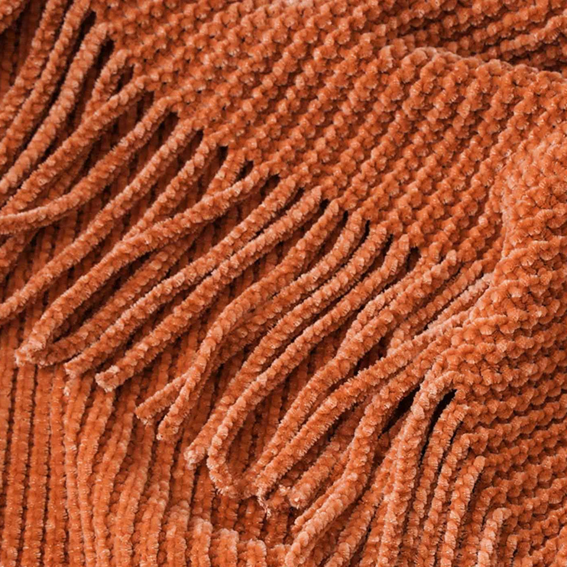 Gros plan de la maille chenille terracotta et des franges du plaid tricoté