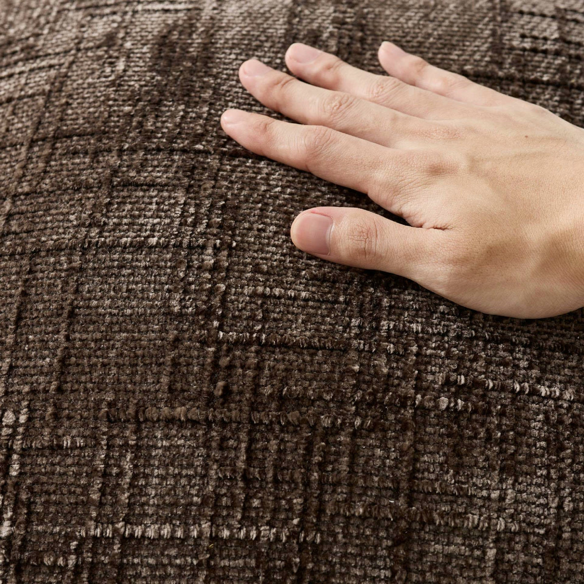 Main posée sur une housse de coussin en chenille café, gros plan du tissage
